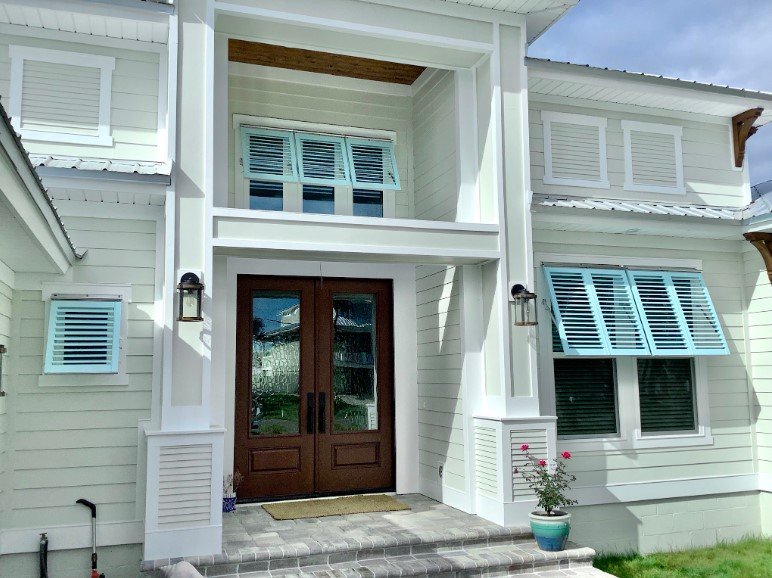 Classic Bahama shutters installed on the exterior windows of a coastal-style home, providing shade and hurricane protection.